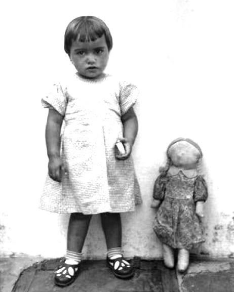 Una niña posando con una muñeca sin rostro.