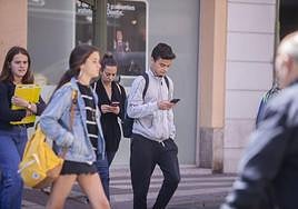 Jóvenes consultando el móvil por la calle.