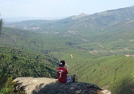Paisaje repleto de árboles en la comarca cacereña de Sierra de Gata, con un joven sentado en la conocida como 'Piedra montá'.