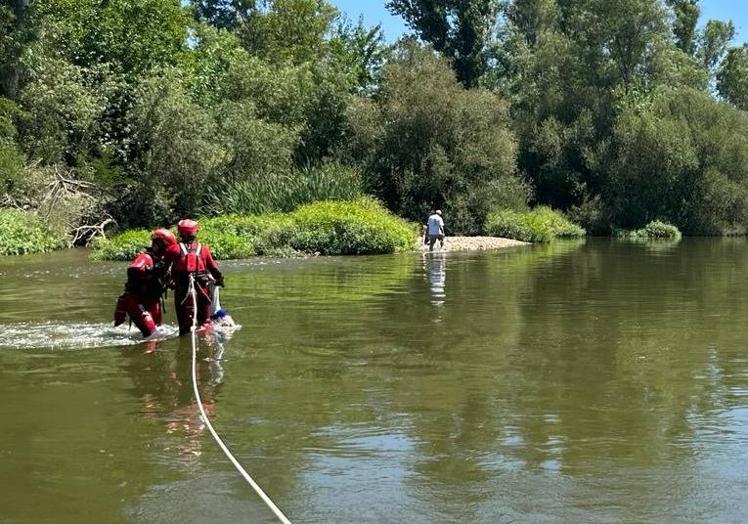 Imagen principal - Momento en el que los bomberos se preparan y trasladan a los miembros de la familia de una orilla a otra.