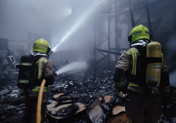 Interior de la nave, con bomberos de la Diputación de Cáceres enfrentando las llamas.