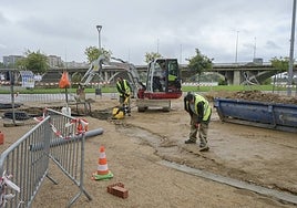 Los operarios preparan las instalaciones para colocar los baños en el parque del río.