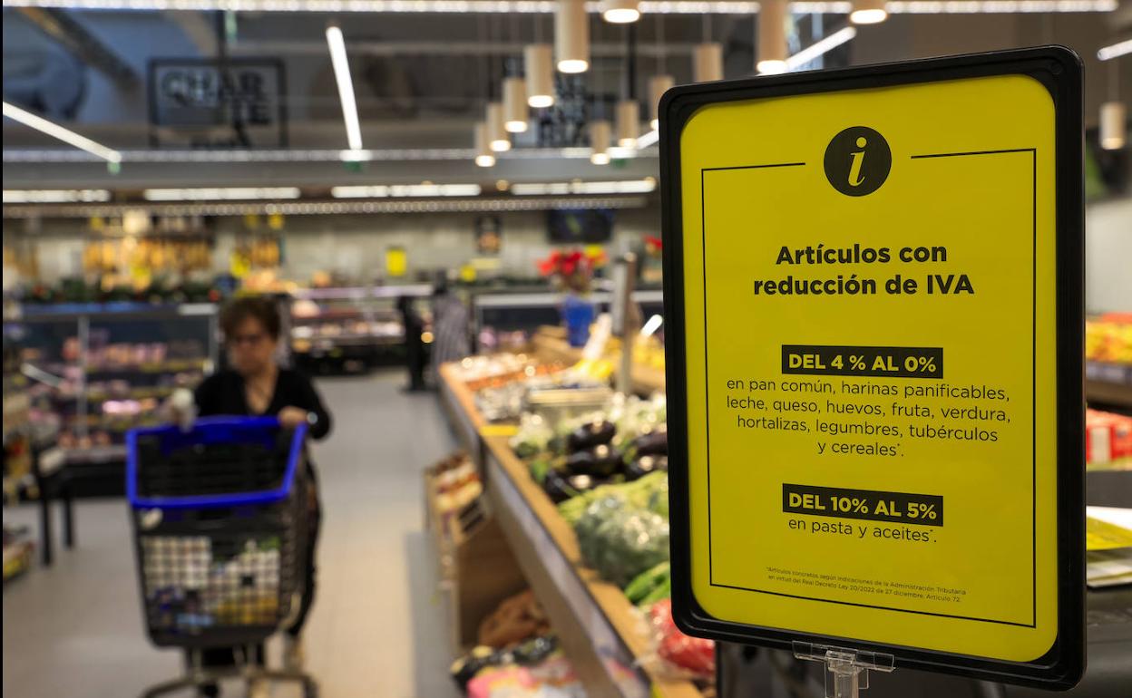 Una mujer hace la compra en un supermercado que muestra la rebaja del IVA de algunos productos.