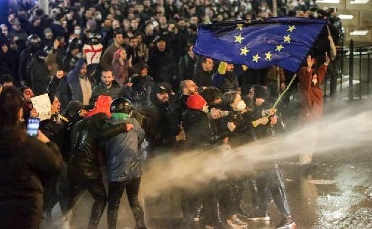 Manifestantes con una bandera de la Unión Europea son rociados por un cañón de agua durante las protestas en Georgia.