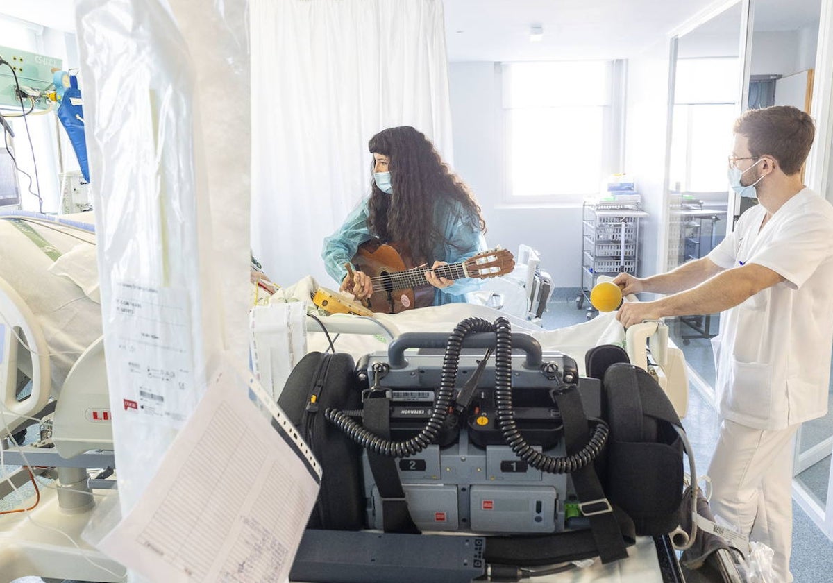 La musicoterapeuta Livia Estévez canta con la guitarra a un paciente ingresado en la UCI. Un enfermero la acompaña con maracas.