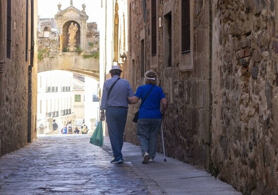 Una pareja camina por la calle Arco de la Estrella, en la Ciudad Monumental de Cáceres, con la Plaza Mayor al fondo.