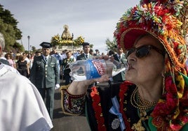 Hizo calor en la procesión de bajada, sobre todo, en el primer tramo. En la imagen, una participante en el desfile ataviada con el traje típico bebe con la Virgen al fondo.