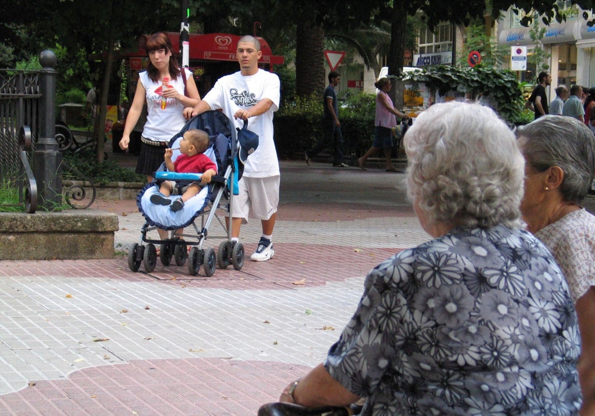 Una pareja pasea con su bebé mientras unas mujeres descansan en Cánovas.