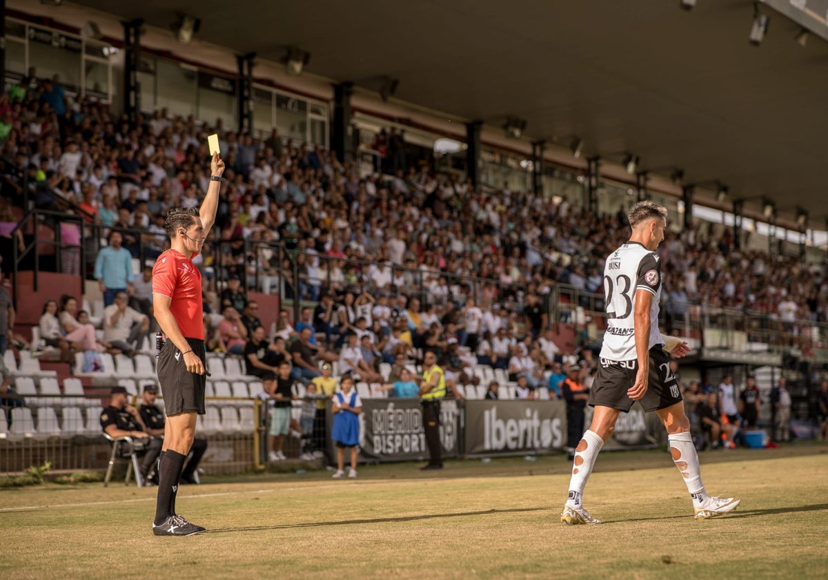 El colegiado Manuel Camacho Garrote mostrando la tarjeta amarilla al jugador del Mérida Busi.