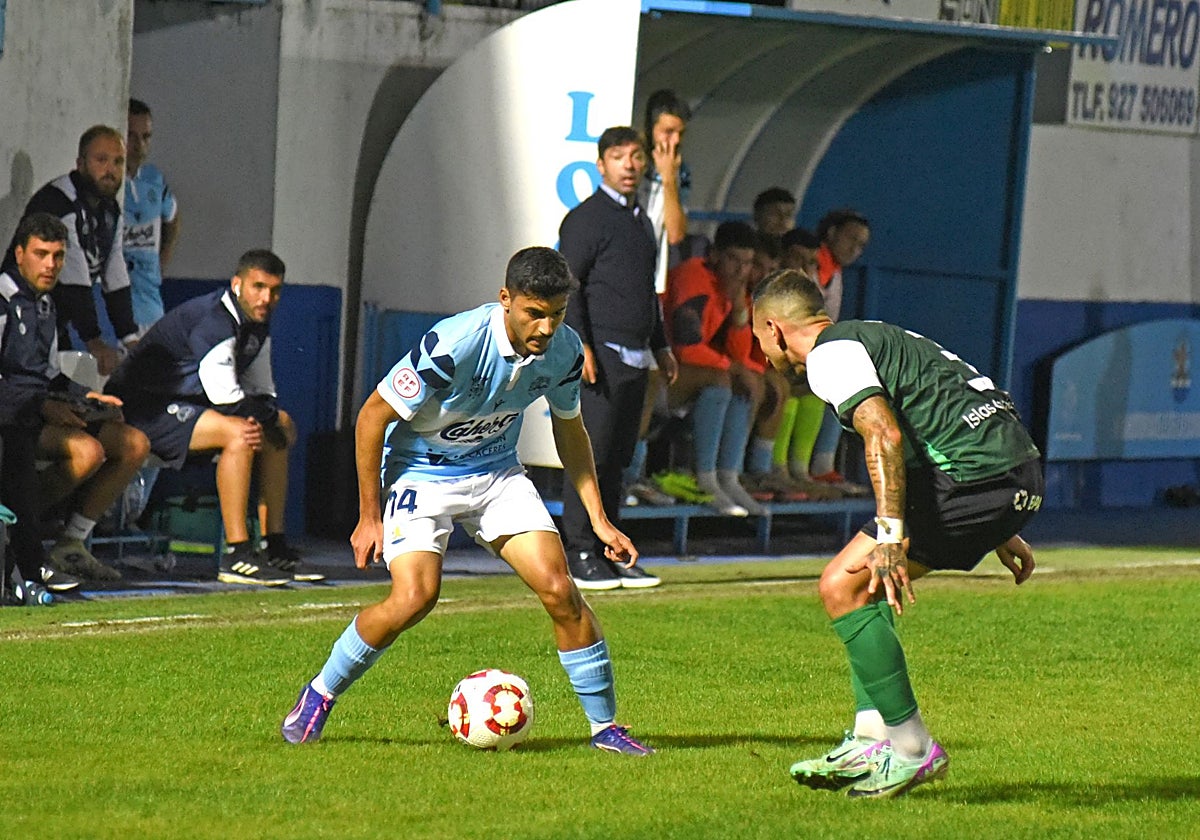 Hamza conduce el balón ante la mirada de Rai Rosa desde el banquillo durante el partido del Coria ante el Atlético Paso.