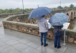 Dos turistas, junto al Puente Romano de Mérida en una jornada lluviosa.