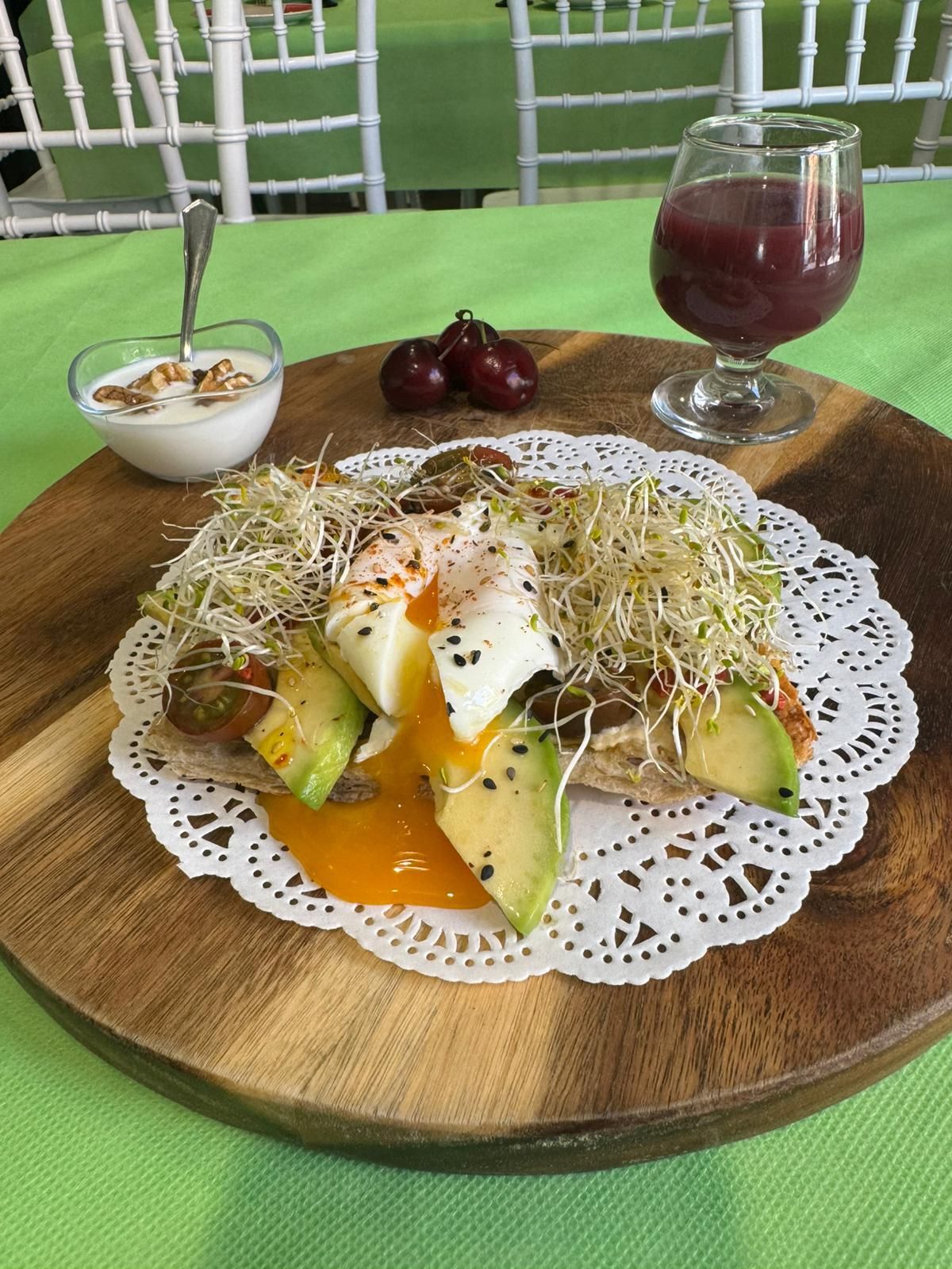 Es una tostada de pan de focaccia de semillas con base de hummus, aguacate, aceite de sésamo, con unos brotes tiernos y huevo a baja temperatura, acompañado de kéfir con nueces y zumo de arándanos azul o remolacha