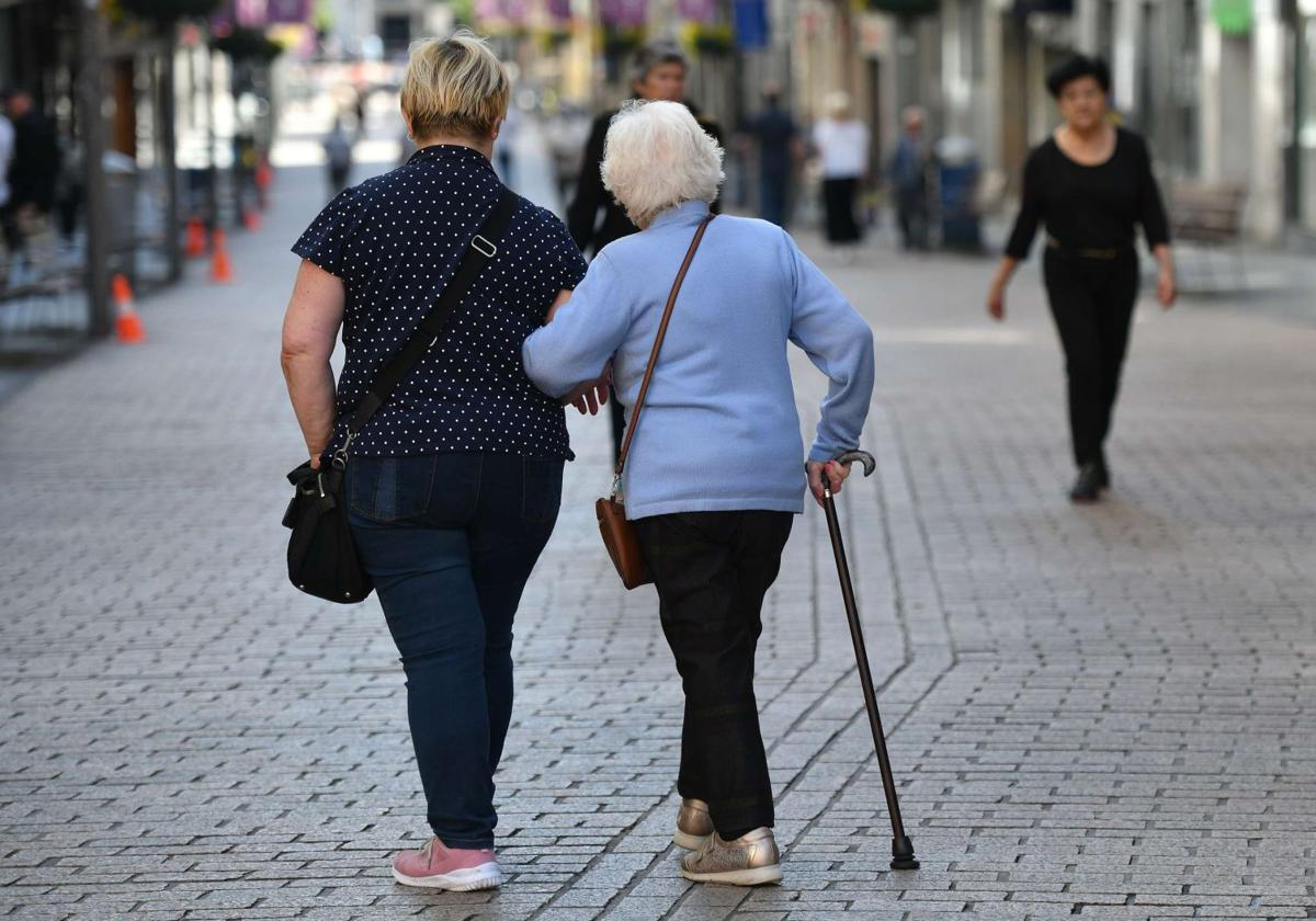 Persona mayor pasea acompañada por la calle.