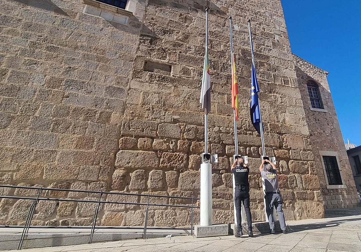Operarios bajan las banderas a media asta en la sede de la Presidencia de la Junta de Extremadura este domingo.