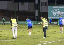 Empleados y colaboradores del Cacereño tratan de tapar los agujeros del césped en el descanso.