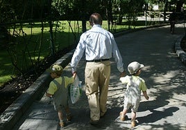 Un abuelo con sus nietos paseando por un parque.