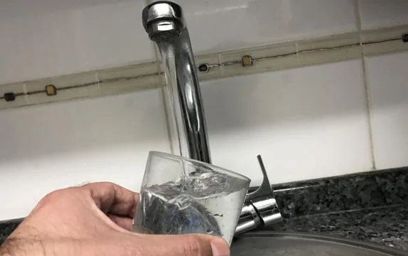 Un hombre se sirve un vaso de agua del grifo. 