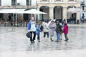 Un grupo de turistas en la Plaza Mayor bien abrigados frente a la lluvia, con veladores vacíos al fondo . ::                             LORENZO CORDERO