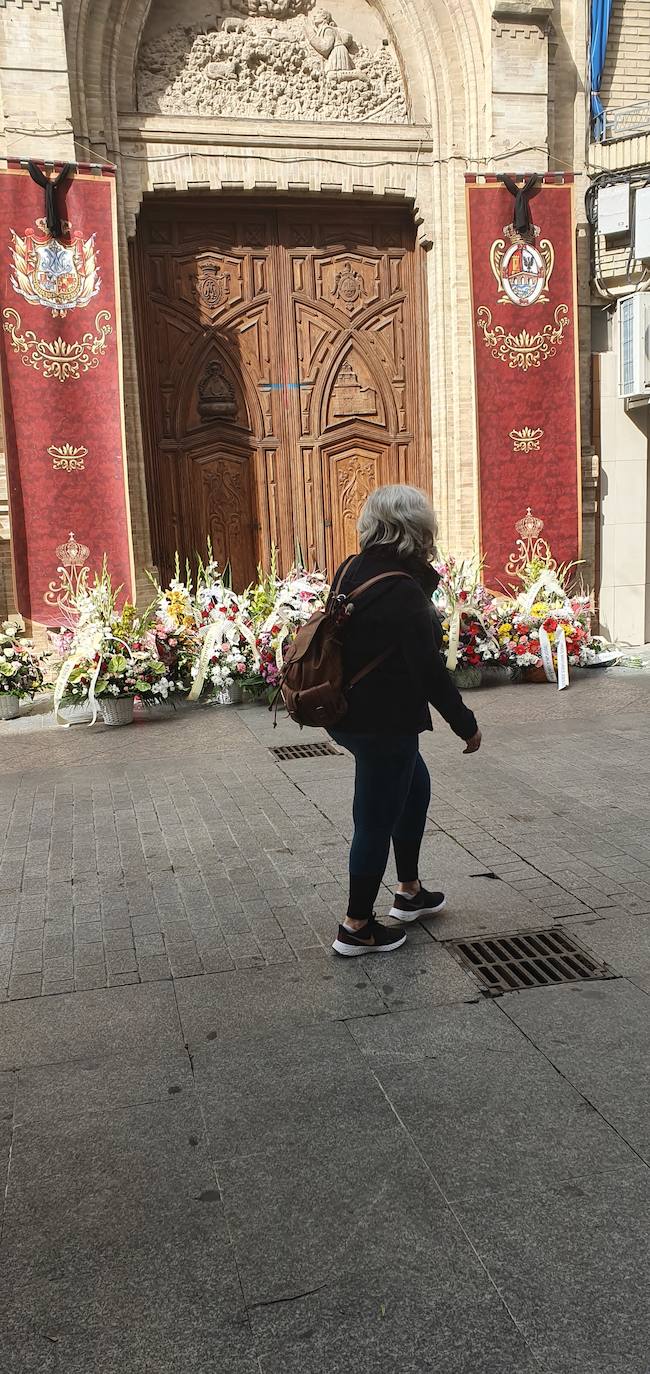 Una mujer pasa delante de los ramos de flores que la Matriz, varias filiales, hermanos mayores y peñas han depositado en la puerta de la ermita de la calle Ollerías. 