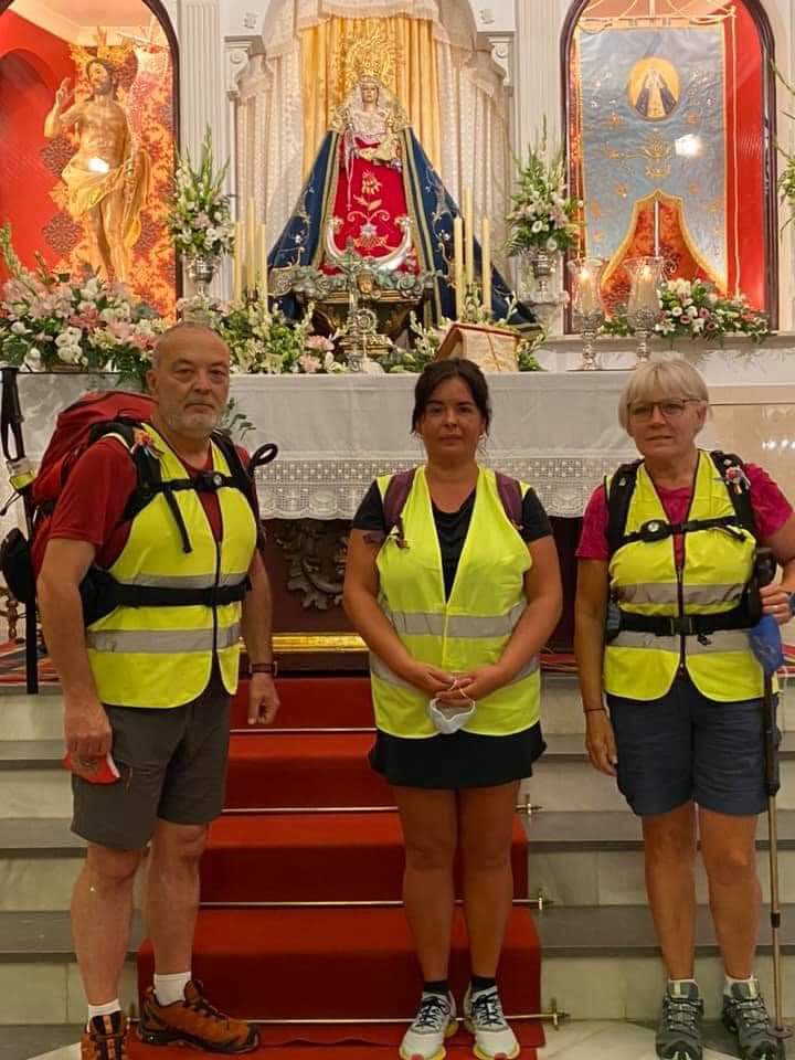 Benito a la izquierda y Flori, a la derecha, posan coin una devota delante de las imágenes del Cristo Resucitado y de la Virgen de la Cabeza de Priego. 