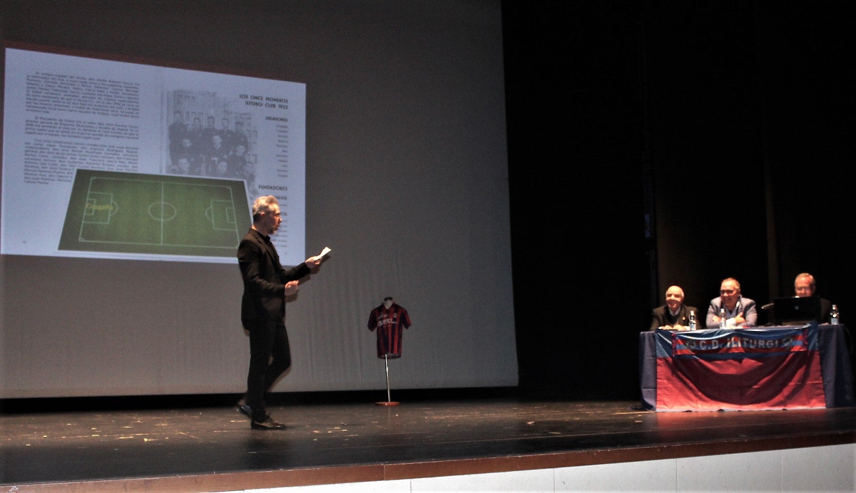 El conductor del acto, Manuel Guerrero, con el fondo del primer equipo del Iliturgi y la familia Utrera. 