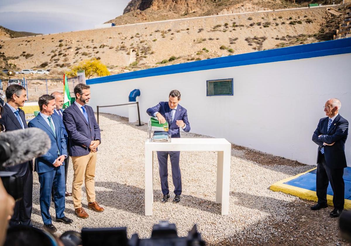 El presidente de la Junta sostiene una bandera de Andalucía ante la atenta mirada de varias autoridades.