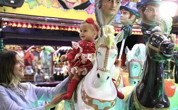 Una niña disfruta del tiovivo junto a su madre.