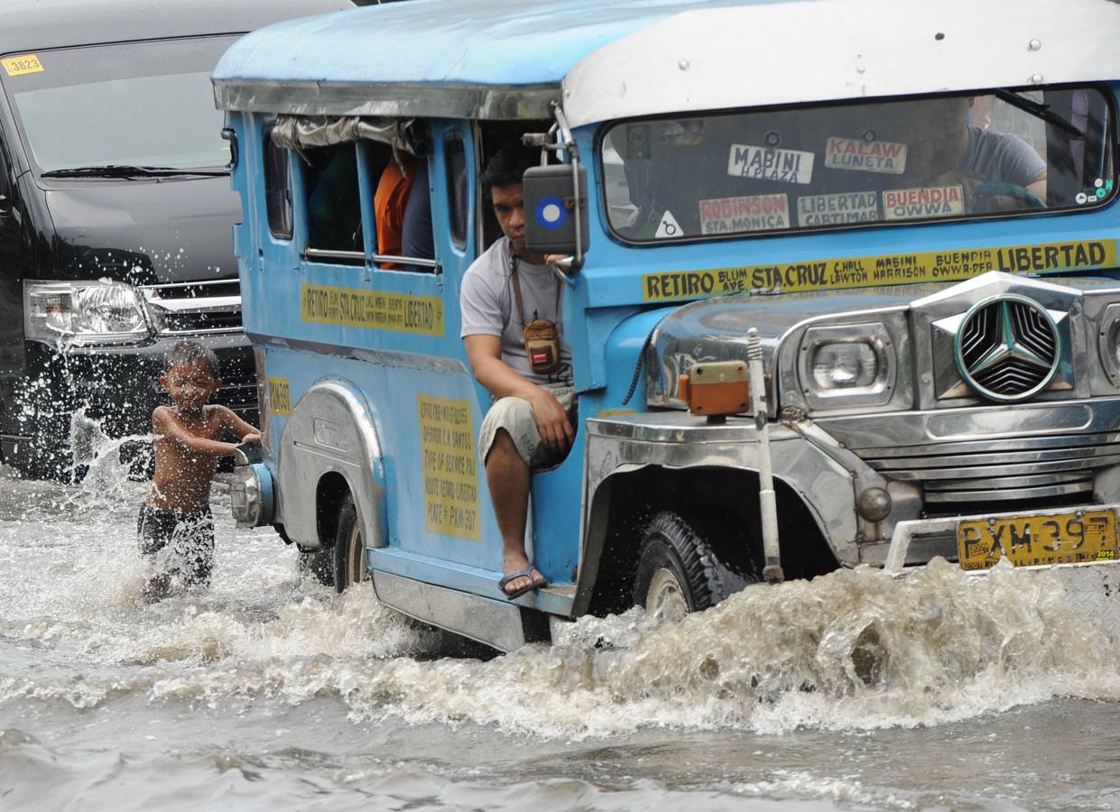 Un niño juega detrás de un pasajero "taxi colectivo" en una calle inundada causado por las fuertes lluvias durante la noche en Manila.