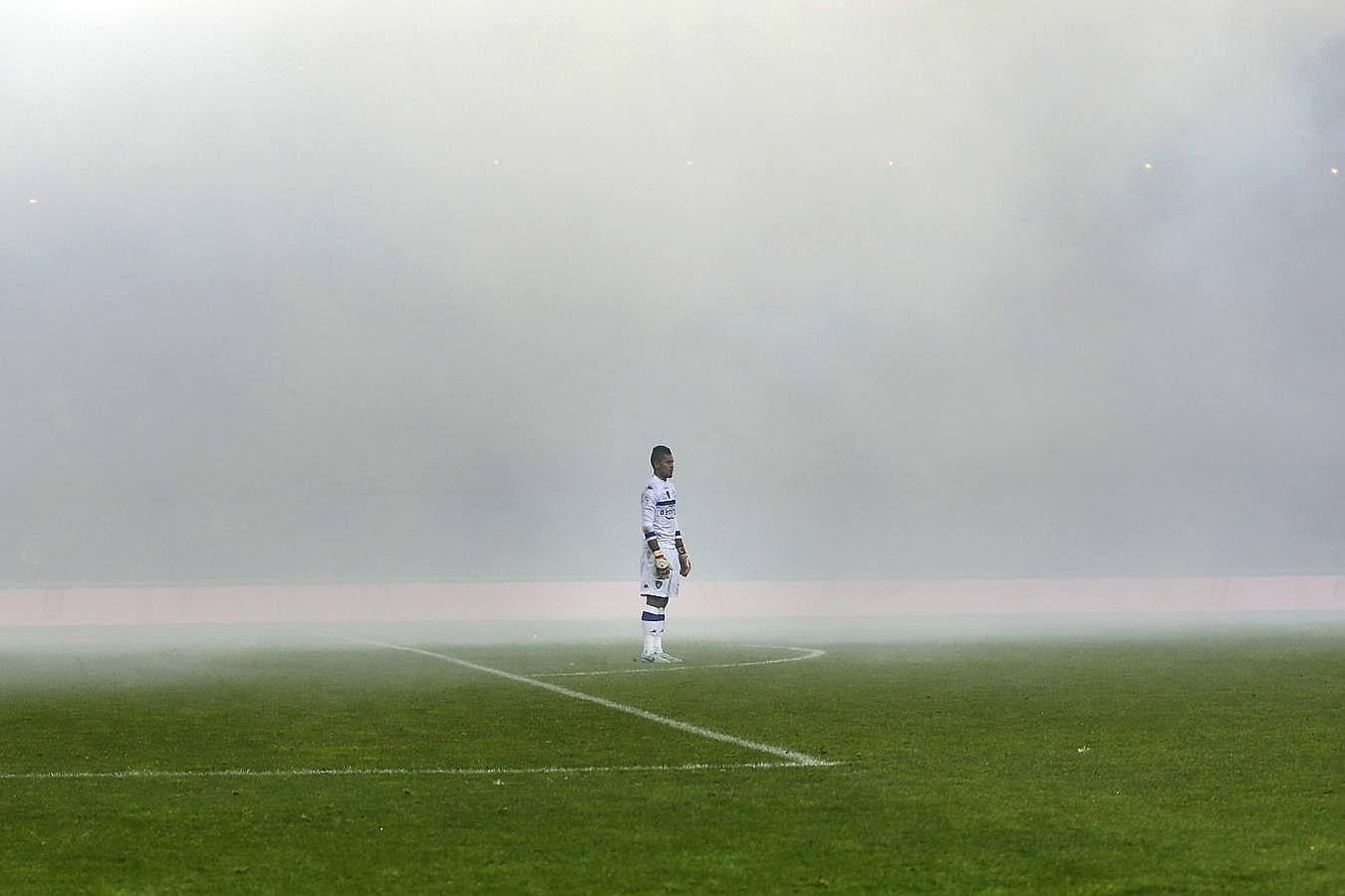 El portero Alphonse Areola se encuentra en medio del humo causado por los fuegos artificiales de los aficionados durante un partido de fútbol.