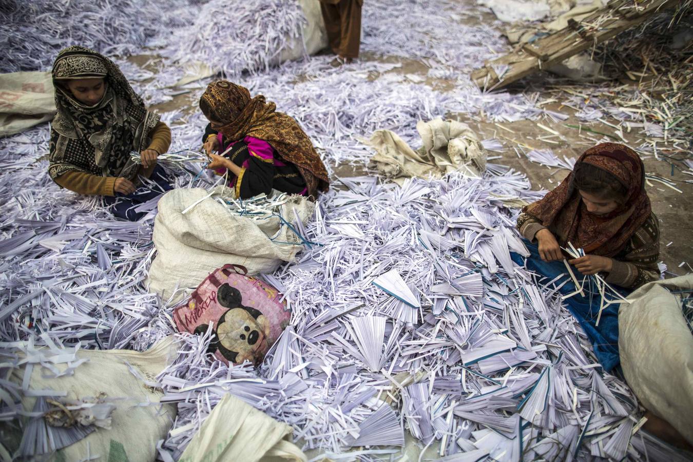 Razia (R), 9, Amna (C), 11 y Saadia, ordenan restos de documentos en tiras antes de ser llevados a una fábrica para ser reciclados en Lahore.