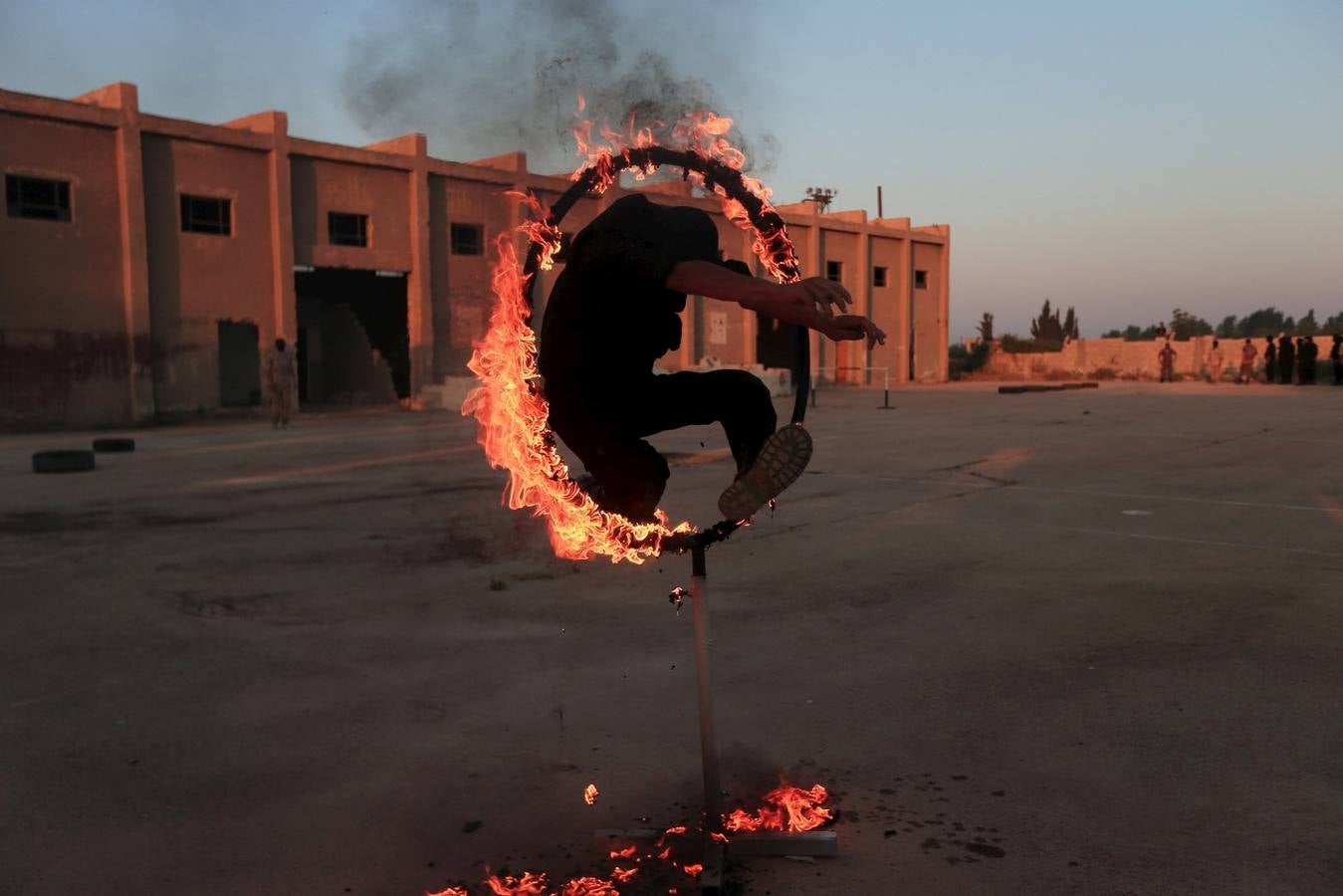 Un combatiente rebelde salta a través de un bucle de fuego como demuestra su habilidad durante una exhibición militar como parte de una ceremonia de graduación en un campamento en el este de al-Ghouta, cerca de Damasco, Siria.