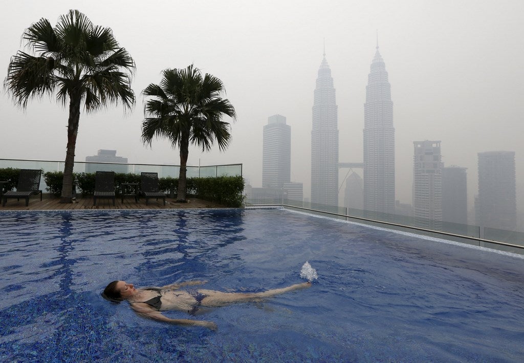 Una mujer nada en una piscina en la azotea frente a las Torres Petronas, envueltas por la bruma, en Kuala Lumpur, Malasia.