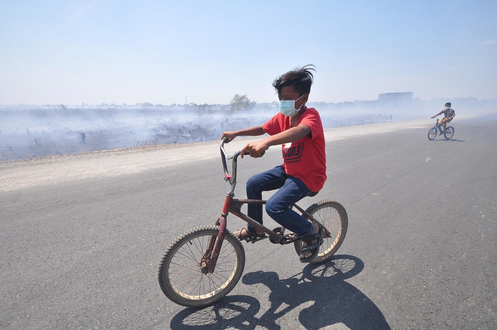 Niños montan sus bicicletas mientras se usan mascarillas para protegerse de la contaminación causada por la bruma en el distrito Banjarbaru de la provincia de Kalimantan del Sur.