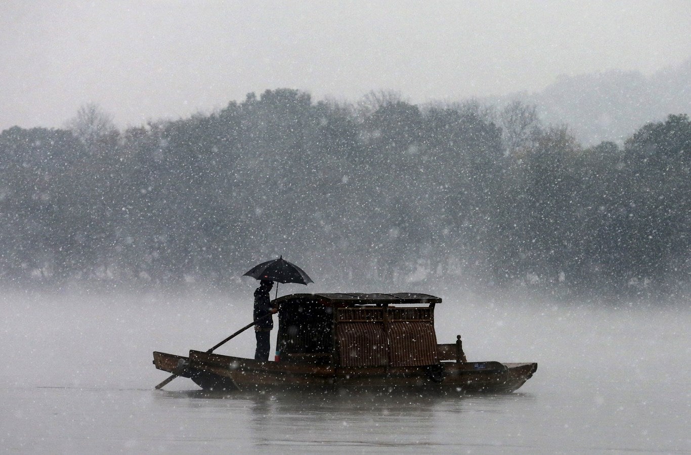 Un hombre sostiene un paraguas para protegerse contra las nevadas mientras rema un barco en el Lago del Oeste en Hangzhou, provincia de Zhejiang, China.