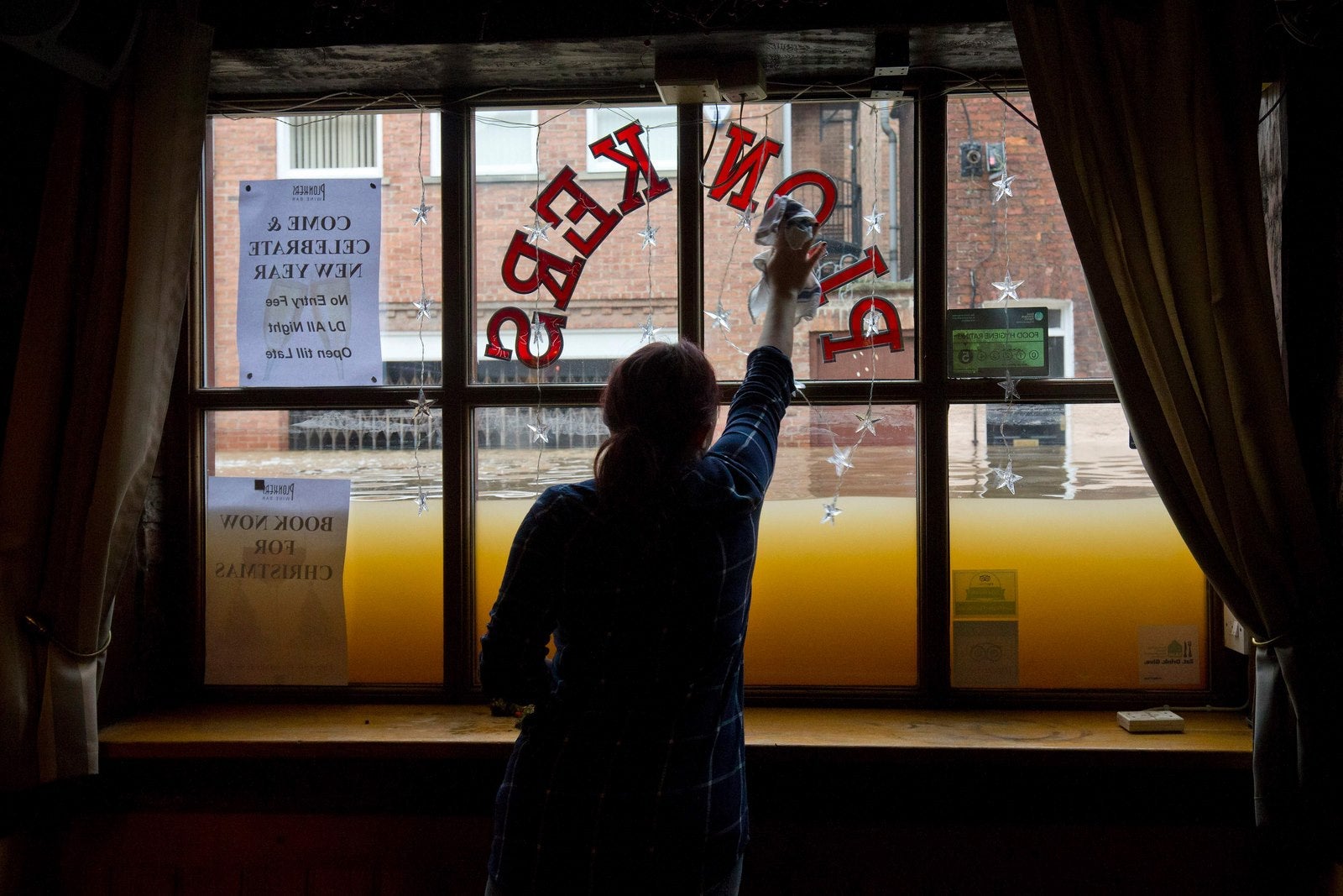 Una mujer limpia la ventana dentro de su bar, ya que las aguas se elevan desde los ríos Ouse y Foss, después de que se desbordaron en York, norte de Inglaterra.