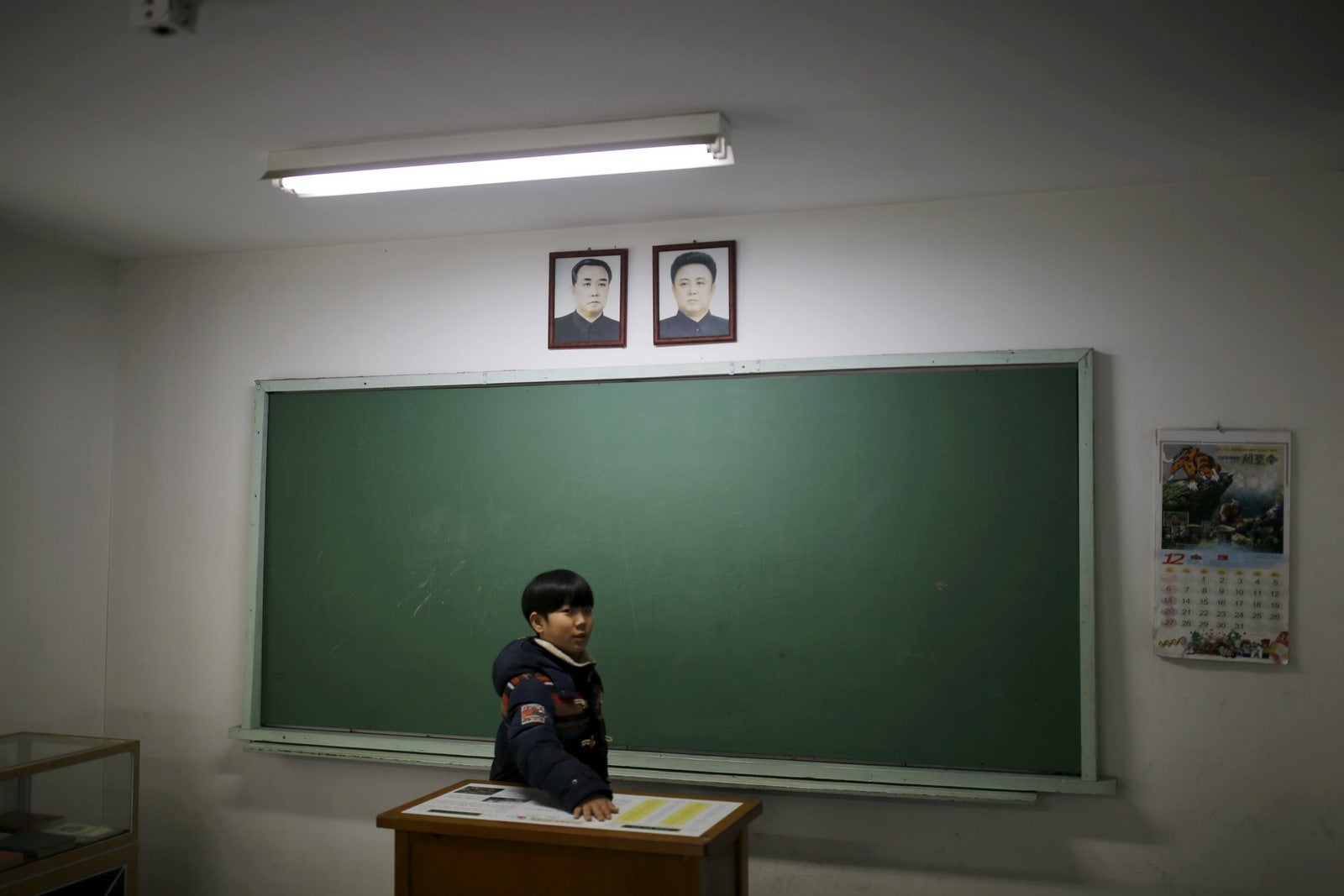 Un niño mira a su alrededor como los retratos del fundador de Corea del Norte Kim Il Sung y su hijo y el difunto líder Kim Jong Il colgar en la pared de un aula de Corea del Norte.