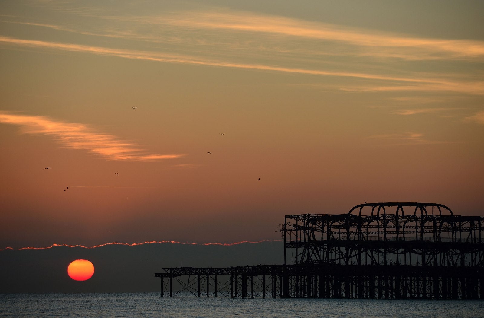 El sol se eleva sobre el horizonte más allá del muelle oeste en Brighton en la costa sur de Inglaterra.