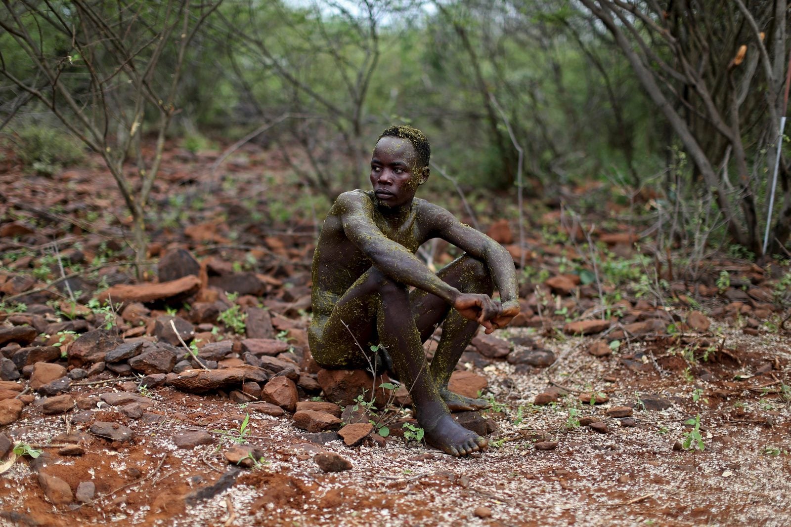 Un hombre pokot se sienta en el suelo después de haber sido untado con el contenido del estómago de un toro por los ancianos durante una ceremonia de iniciación en el condado de Baringo, Kenia.