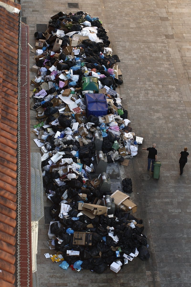 Un camarero empuja un cubo de basura más allá de una pila de bolsas de basura en una calle durante una huelga de recolectores de basura de la compañía de gestión de residuos Limasa, que han estado en huelga desde el 1 de marzo contra los recortes salariales, y para exigir mejores condiciones de trabajo, en el centro de Málaga, el sur de España