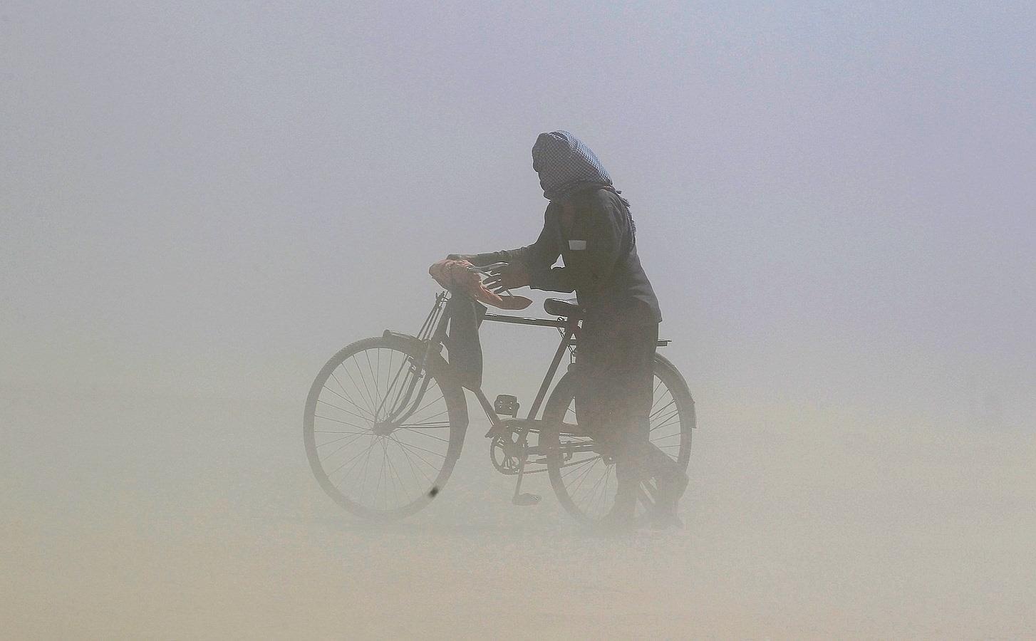 Un hombre cubre su cara mientras que empuja una bicicleta a través de una tormenta de polvo en las orillas del río Ganges en Allahabad, India.