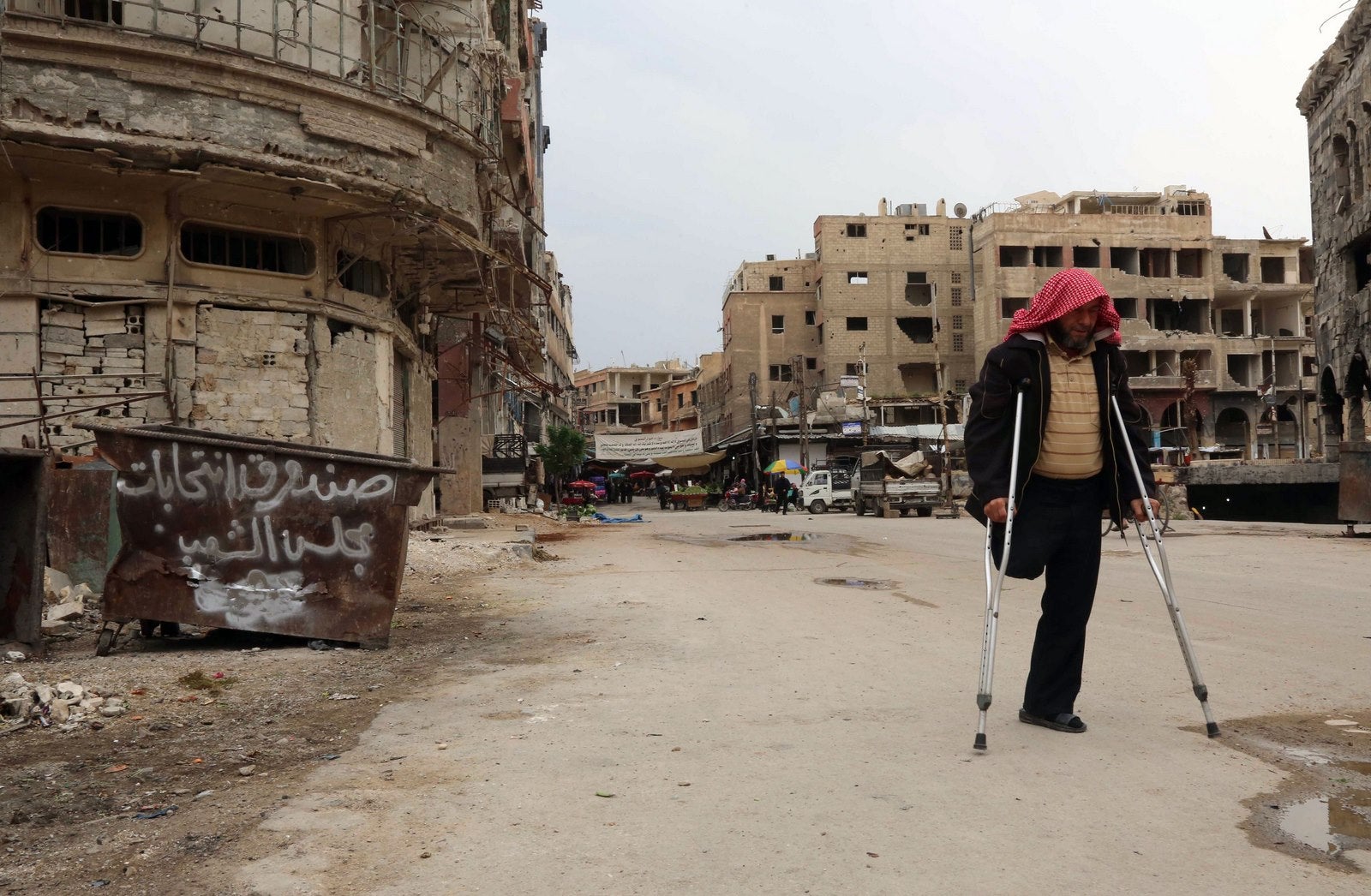 Un hombre herido pasa junto a graffitis anti-elección que describe el cubo de la basura como urnas para las elecciones parlamentarias en la ciudad controlada por los rebeldes de Douma en las afueras de la capital, en protesta a las elecciones parlamentarias