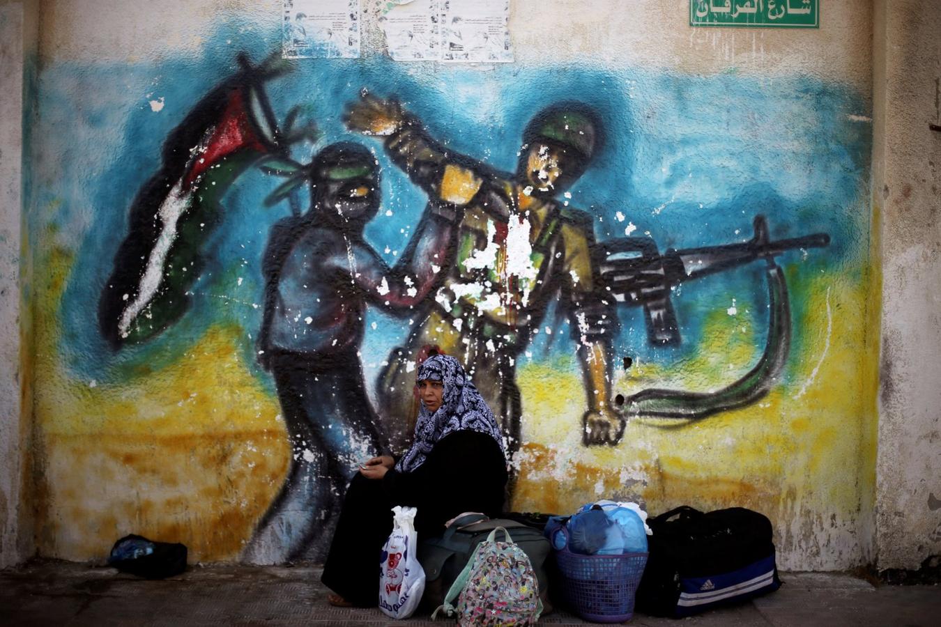 Una mujer se sienta delante de un mural mientras espera un permiso de viaje para cruzar a Egipto a través del paso fronterizo de Rafah