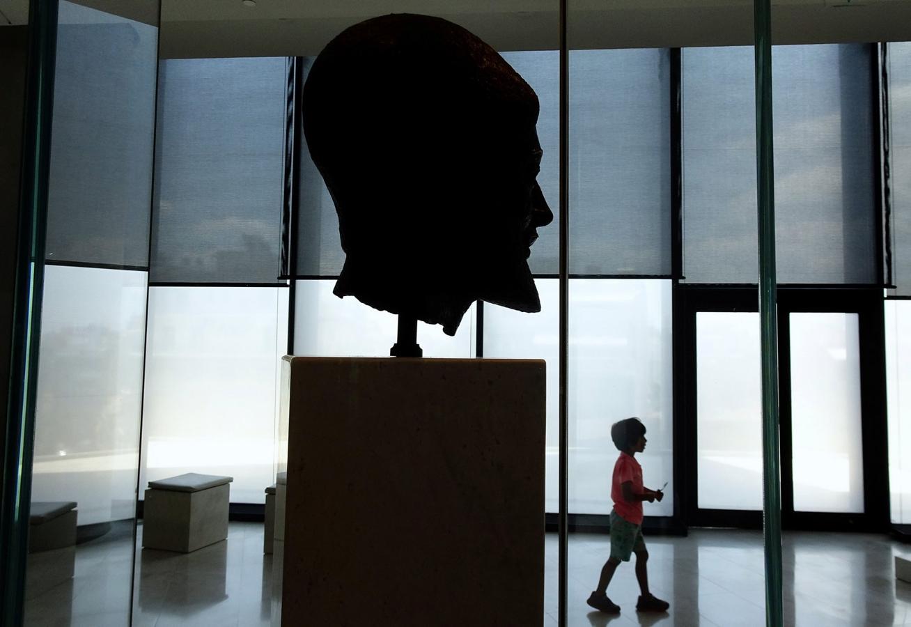 Un joven turista camina por una cabeza de bronce 470-480 aC de un hoplita barba (soldado) en el interior del Museo de la Acrópolis en Atenas, Grecia