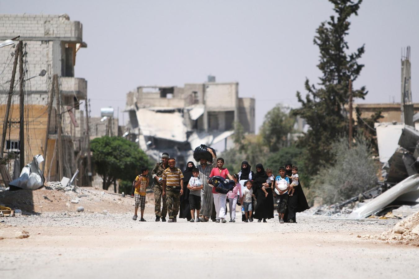 Combatientes de las Fuerzas Democráticas Siria caminan con las personas que huyeron de sus hogares debido a los últimos enfrentamientos.