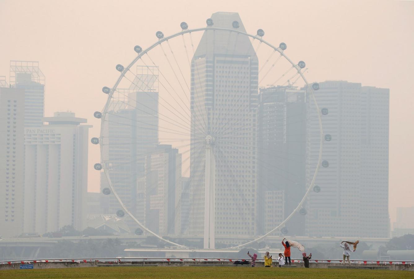 La gente toma fotos cerca de la rueda observatorio Singapore Flyer envuelta por la bruma