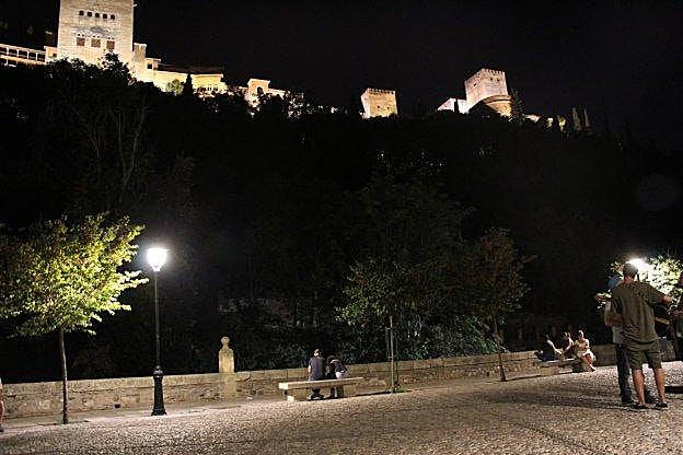Varias personas disfrutan de las vistas nocturnas hacia la Alhambra desde el Paseo de los Tristes.