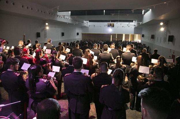Una banda interpreta una marcha procesional ante un auditorio lleno.