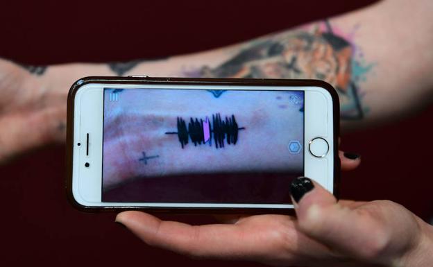 Hanna Washlake sostiene un telefono con las ondas de su tatuaje. 
