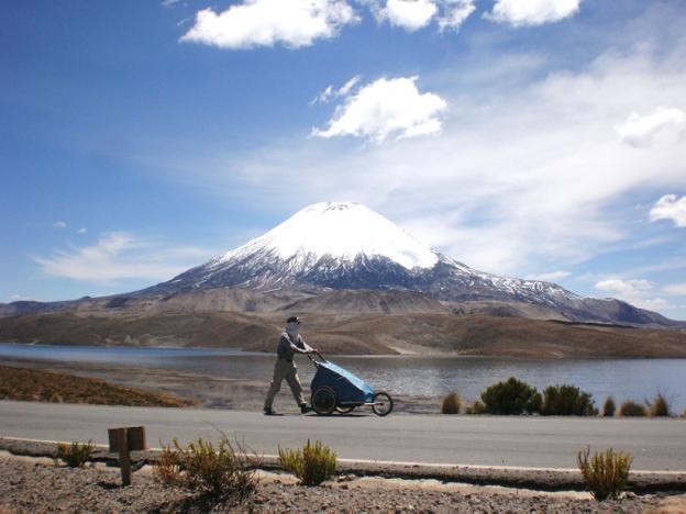 Nacho camina con su inseparable carrito frente a un volcán nevado en el lago Chungará, en Chile.