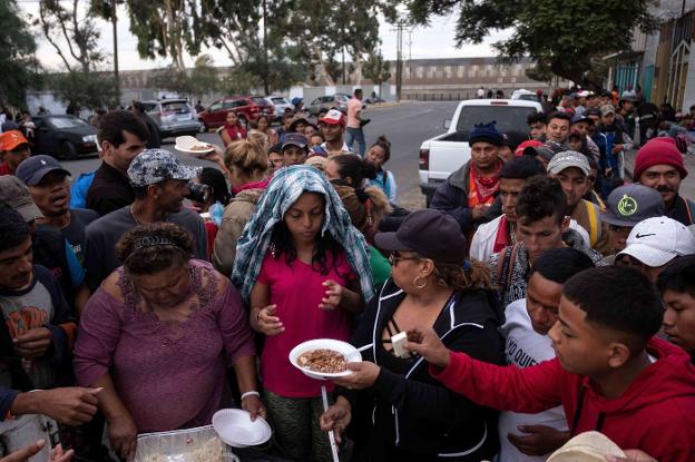 Inmigrantes, la mayoría llegados de Honduras, recogen platos de frijoles en una olla comunal en la frontera de Tijuana.